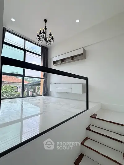 Elegant modern interior with large windows and chandelier, featuring a sleek staircase and outdoor view.