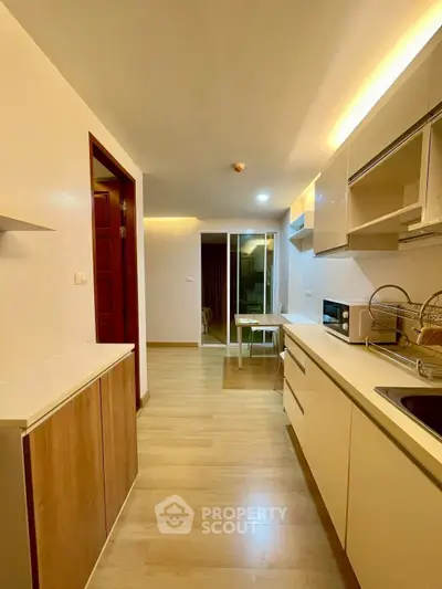 Modern kitchen with sleek cabinets and wooden flooring, featuring a microwave and dish rack.