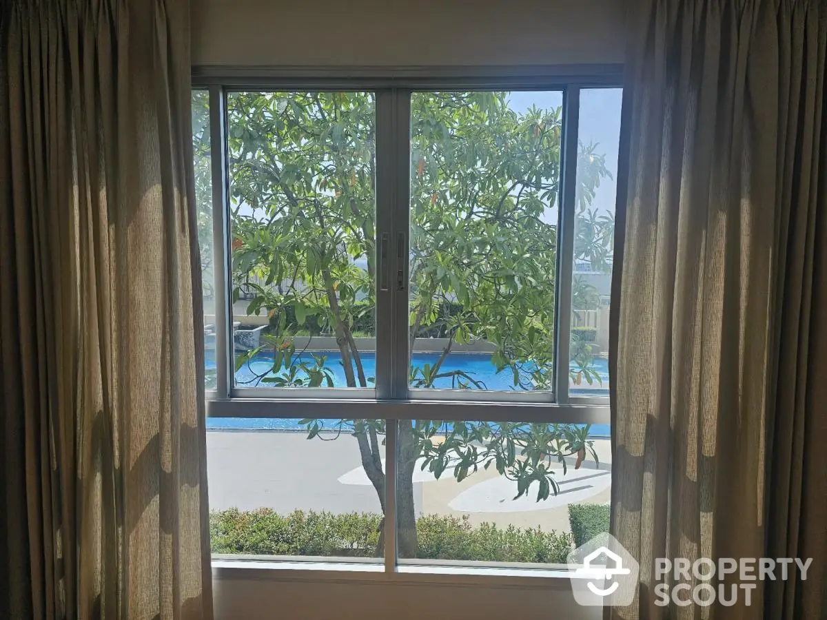 Serene pool view through window with lush greenery and curtains