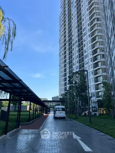 Modern high-rise building with paved driveway and lush greenery.