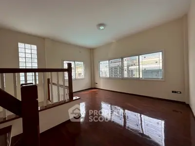 Spacious sunlit room with polished wooden floors and large windows