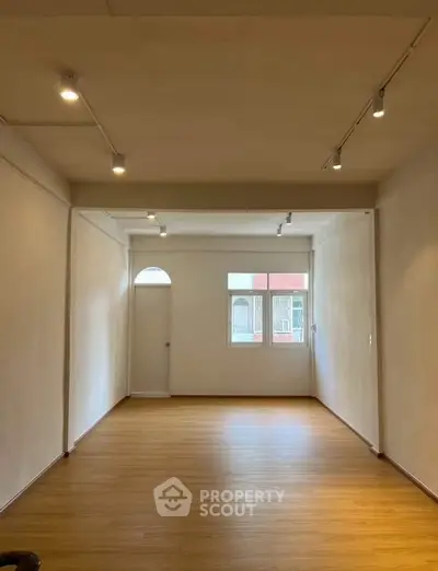 Spacious empty room with wooden flooring and track lighting, ideal for customization.