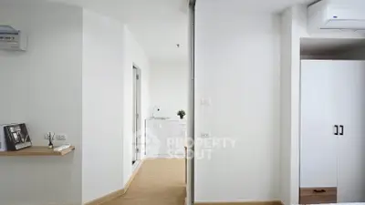 Modern minimalist interior with white walls and wood flooring, featuring a compact kitchenette.
