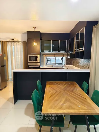 Modern kitchen with sleek black cabinetry, built-in oven, and elegant dining area with green chairs.