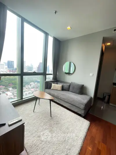 Modern living room with large windows and city view, featuring a cozy gray sofa and stylish decor.