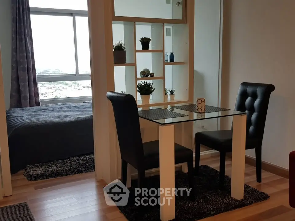 Modern dining area with glass table and black chairs, adjacent to cozy bedroom with city view.