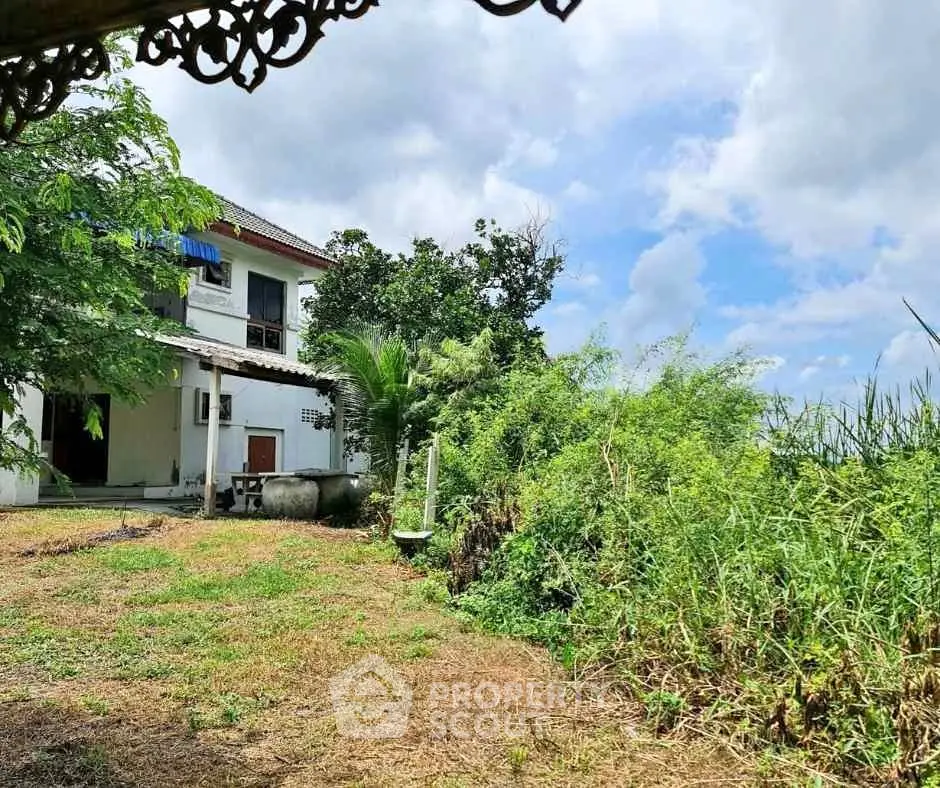 Charming countryside house with lush greenery and spacious outdoor area under a bright blue sky.