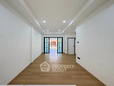 Spacious modern living room with wooden flooring and large glass doors leading to balcony.