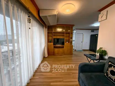 Spacious living room with wooden flooring and modern decor, featuring large windows and stylish furniture.