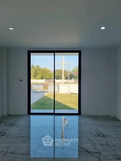 Spacious room with large glass doors offering a serene garden view, featuring elegant marble flooring.