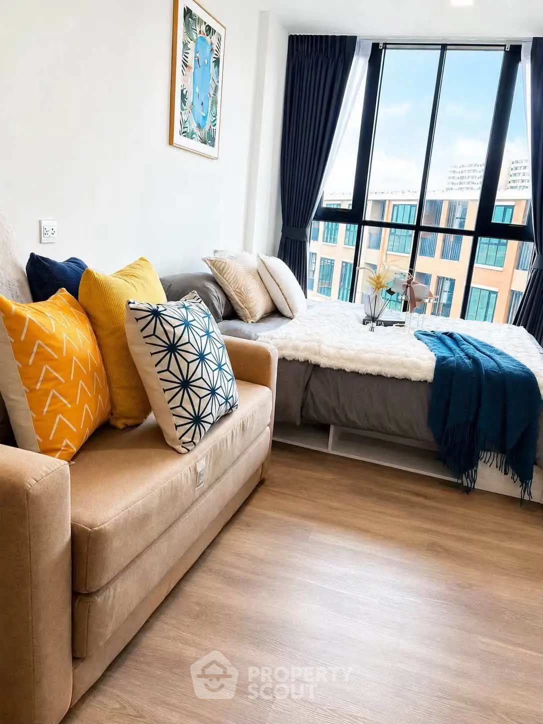 Modern studio apartment with cozy sofa and stylish bed, featuring large windows and vibrant decor.