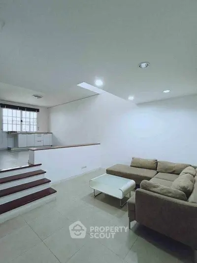 Spacious living room with modern sofa and open layout leading to kitchen area.