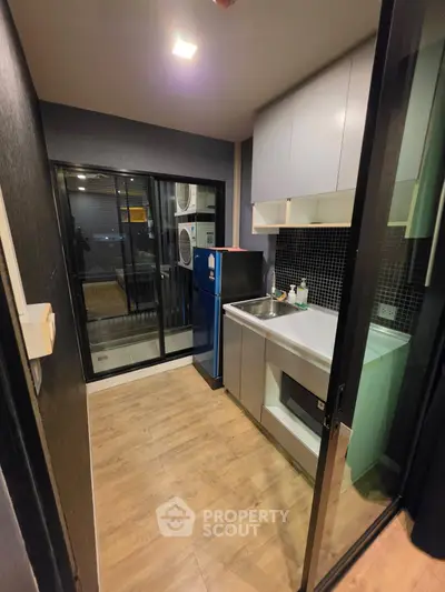 Modern kitchen with sleek cabinetry and glass sliding door, featuring a compact layout and stylish design.