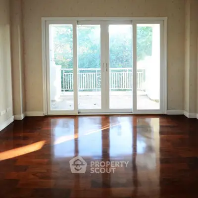 Spacious room with polished wooden floors and large glass doors leading to a balcony.