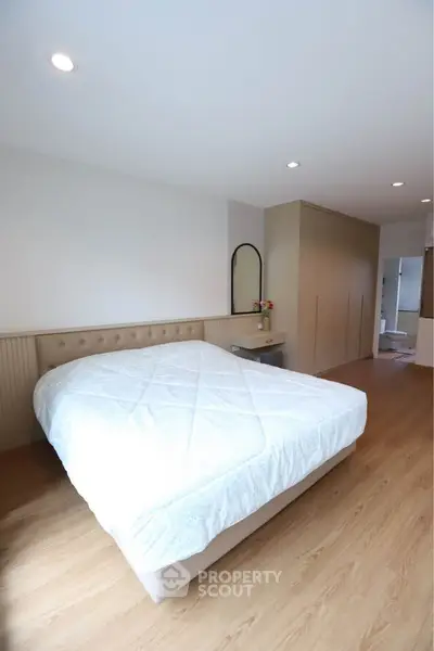 Spacious bedroom with modern design and ample natural light, featuring a cozy bed and elegant wooden flooring.