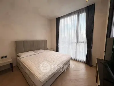 Spacious bedroom with large window and modern furnishings in a high-rise apartment.