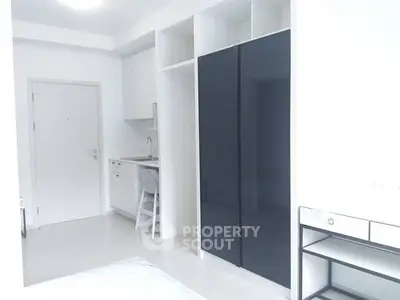Modern minimalist apartment interior with sleek black wardrobe and compact kitchen area.