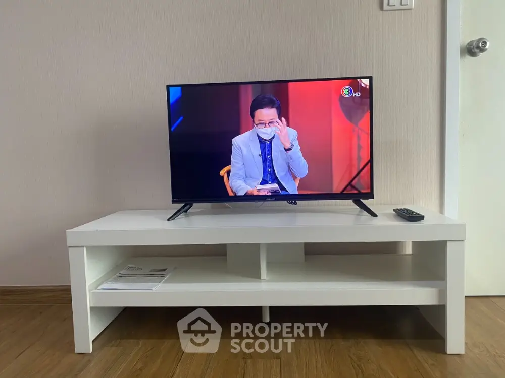 Modern living room with sleek TV setup on white stand, wooden flooring, and minimalist decor.