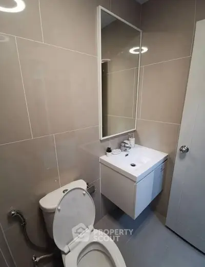 Modern bathroom with sleek fixtures and neutral tiles, featuring a wall-mounted sink and large mirror.