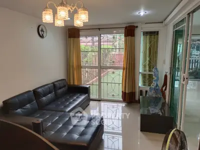 Stylish living room with black leather sofa and elegant chandelier, featuring large windows for natural light.