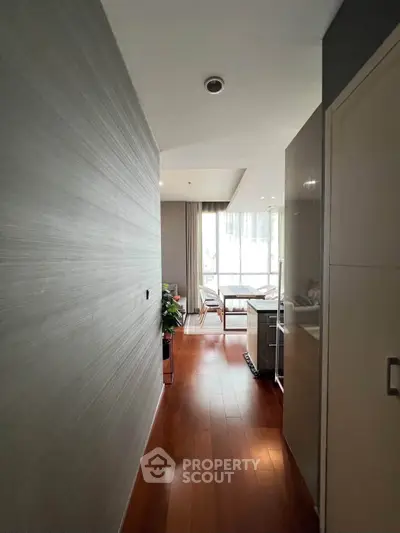 Modern apartment hallway leading to a bright living area with wooden flooring and large windows.