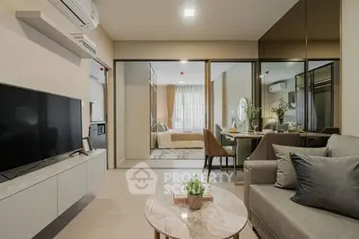 Modern living room with open layout to dining and bedroom, featuring sleek furniture and neutral tones.