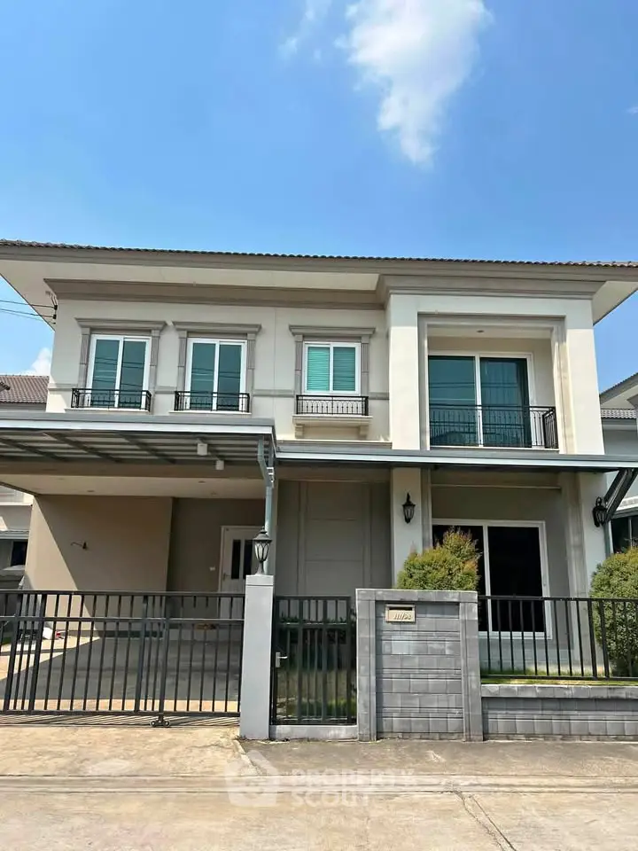 Modern two-story house with balcony and gated driveway in a suburban neighborhood.