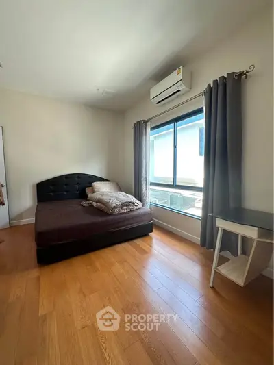 Spacious bedroom with wooden flooring, large window, and modern air conditioning unit.