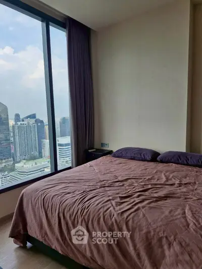 Luxurious bedroom with stunning city view from floor-to-ceiling window in high-rise apartment.