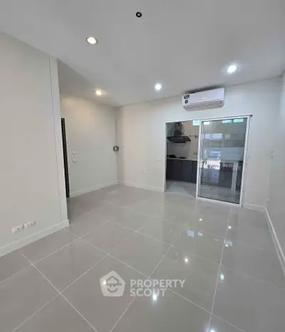 Modern empty living room with glossy tiled floors and air conditioning unit, adjacent to a sleek kitchen area.