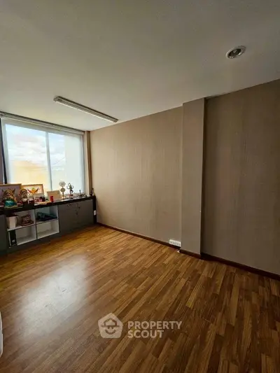 Spacious room with wooden flooring and large window, perfect for customization.