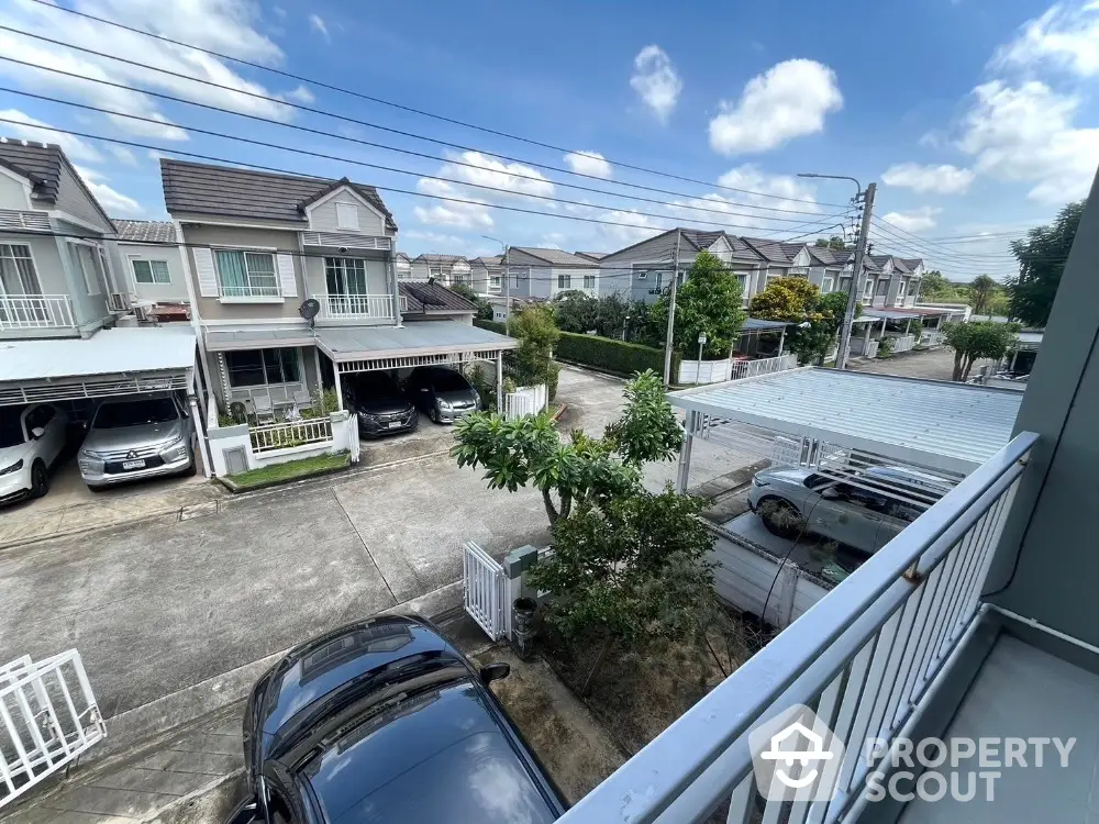 Charming suburban neighborhood view from balcony with parked cars and row houses under blue sky.