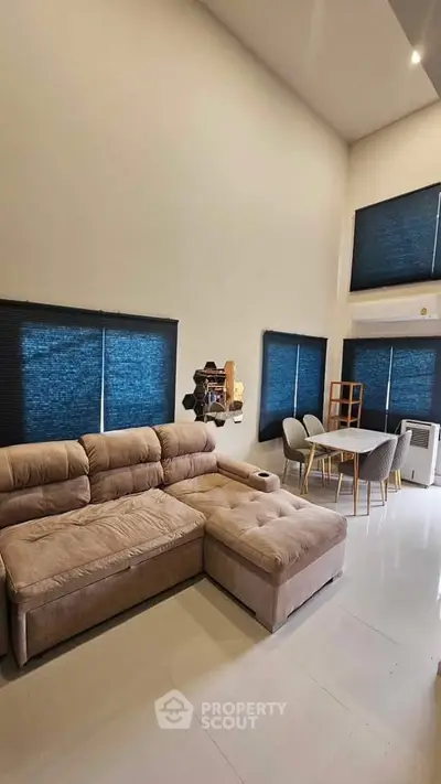 Spacious modern living room with plush sectional sofa and dining area, featuring high ceilings and large windows.
