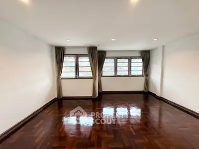 Spacious empty room with polished wooden floors and large windows, perfect for customization.