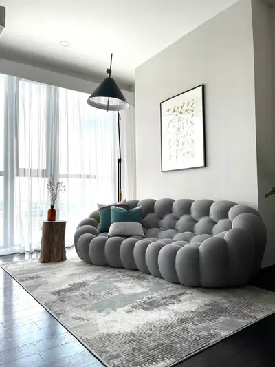 Modern living room with stylish gray sofa, floor lamp, and large window with sheer curtains.