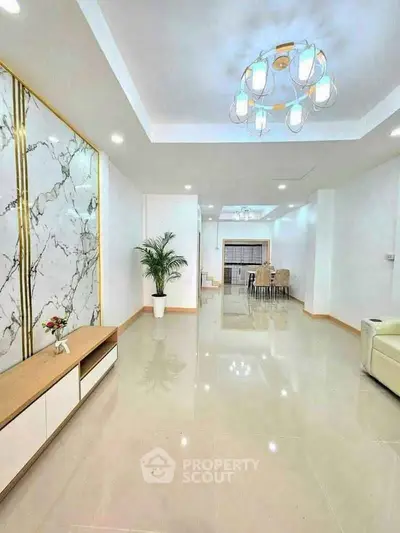 Spacious modern living room with elegant chandelier and marble accent wall, perfect for luxury living.