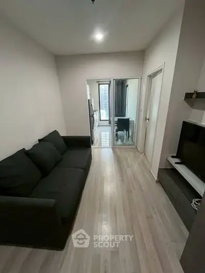 Modern living room with sleek black sofa and TV, leading to a bright dining area.