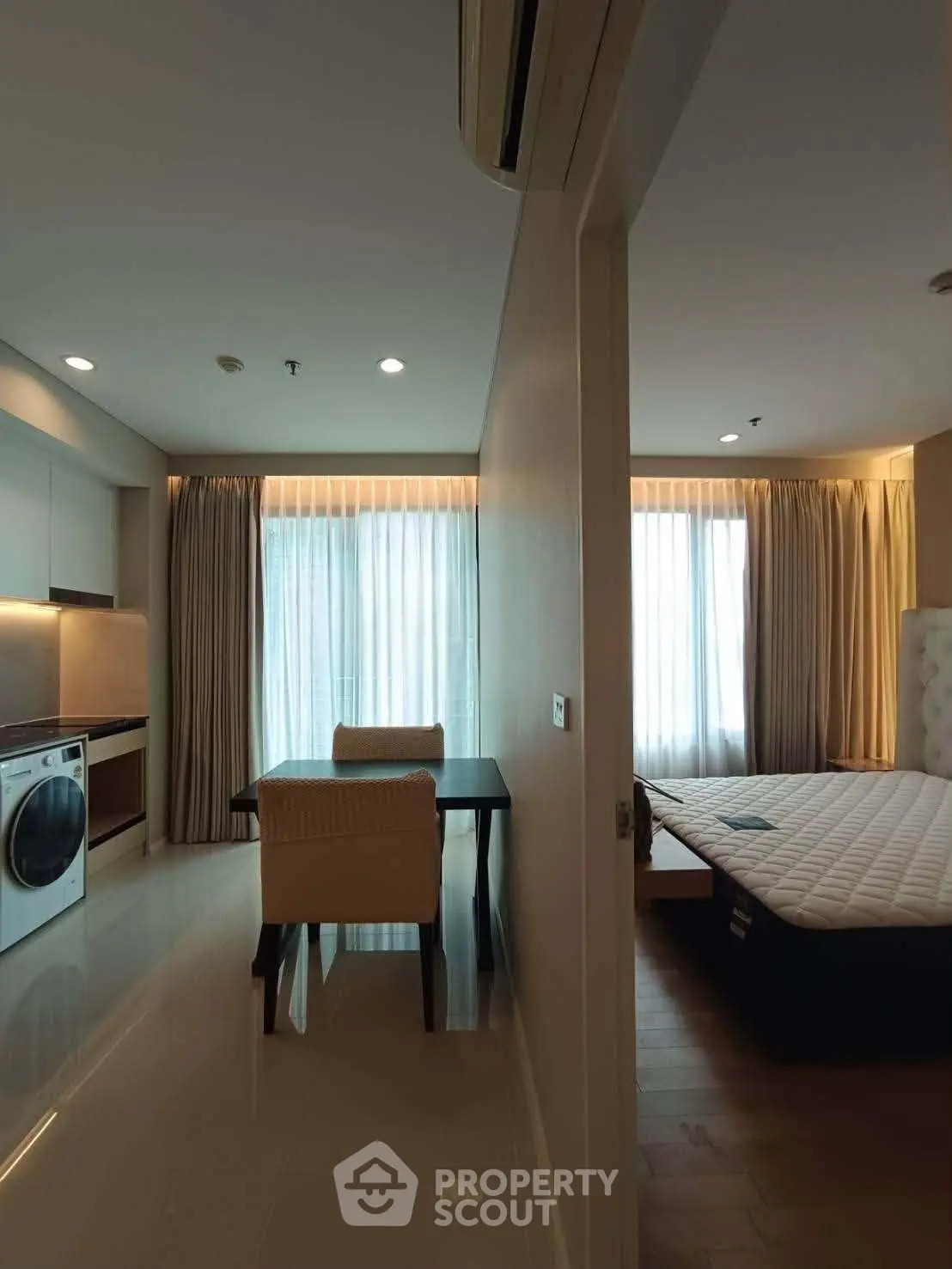 Modern apartment interior with dining area and bedroom, featuring sleek furniture and natural light.