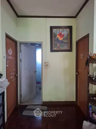 Cozy interior hallway with wooden flooring and colorful parrot artwork, leading to a bathroom and other rooms.