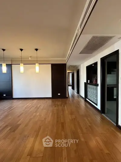 Spacious modern living room with wooden flooring and elegant lighting fixtures.