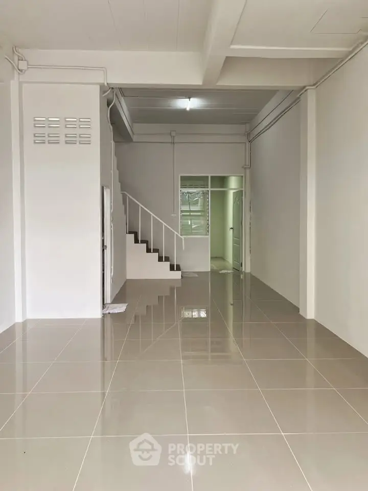 Spacious open-plan interior with sleek tiled flooring and modern staircase, perfect for versatile living or office space.