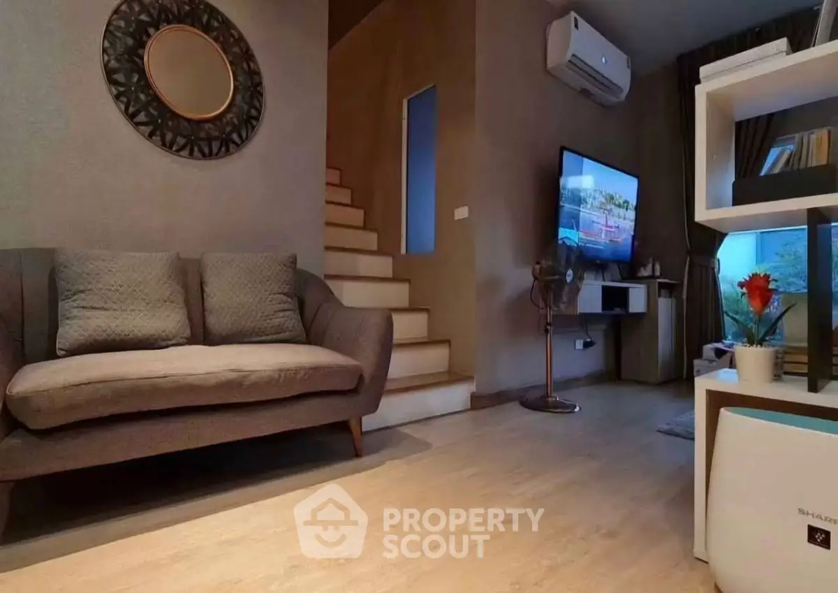 Cozy living room with modern decor and staircase, featuring a wall-mounted TV and air conditioning.