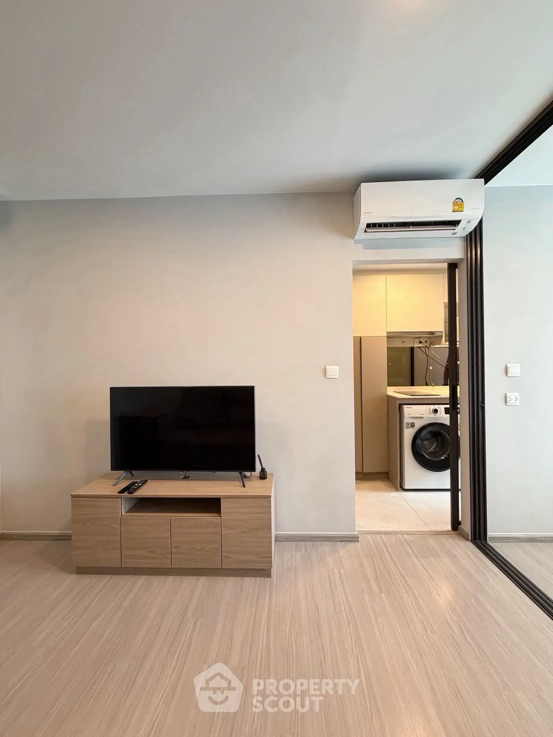 Modern living room with TV and air conditioning, adjacent to laundry area with washing machine.