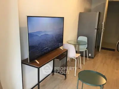 Modern living room with sleek TV, stylish furniture, and stainless steel fridge in open layout.