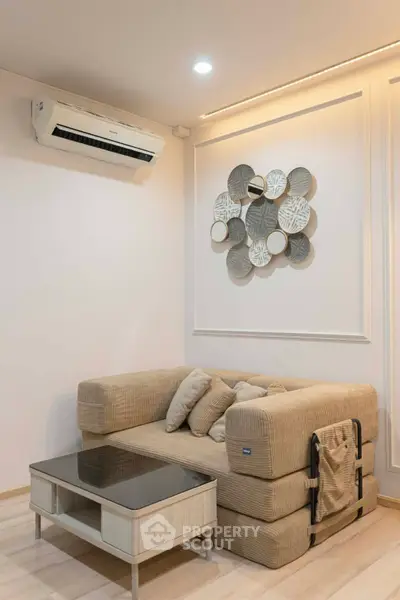 Modern living room with stylish decor and air conditioning, featuring a cozy beige sofa and elegant wall art.