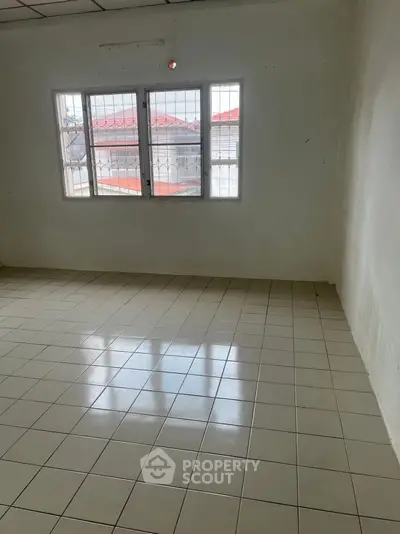 Spacious empty room with tiled floor and barred windows, ready for customization.