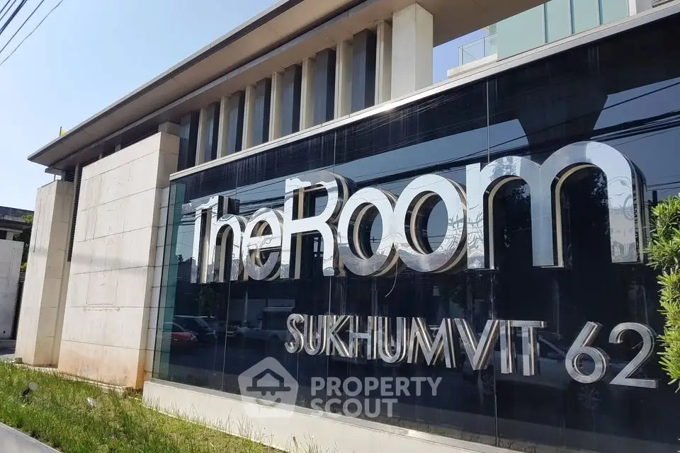 Modern building exterior with sleek signage at The Room Sukhumvit 62, showcasing contemporary architecture.