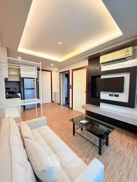 Modern living room with sleek design, featuring a cozy sofa, wall-mounted TV, and open kitchen layout.