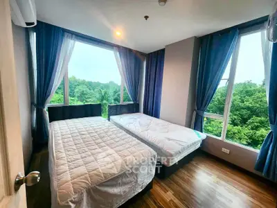 Spacious bedroom with large windows offering lush green views, featuring two cozy beds and elegant curtains.