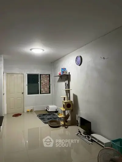 Spacious living room with glossy tiled floors and minimalistic decor, featuring a cat tree and wall clock.